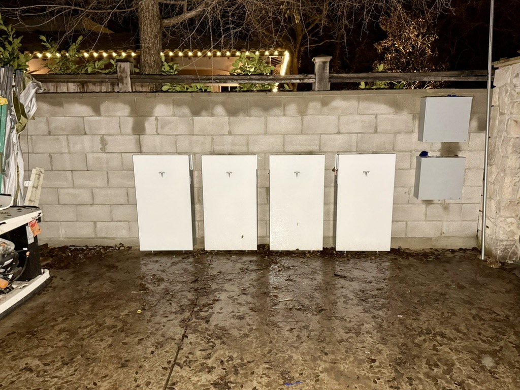 Four Tesla Powerwalls installed along a cinderblock wall